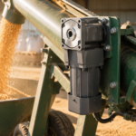 Compact right-angle AC gear reducer motor mounted on a grain auger conveyor in a dusty farm workshop, conveying grain.